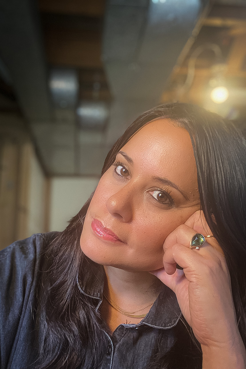 Image of a tan person with shoulder-length dark hair resting their head on their hand