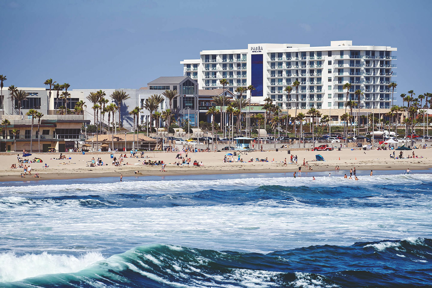 Image of waves crashing into the beach with a hotel building in the background