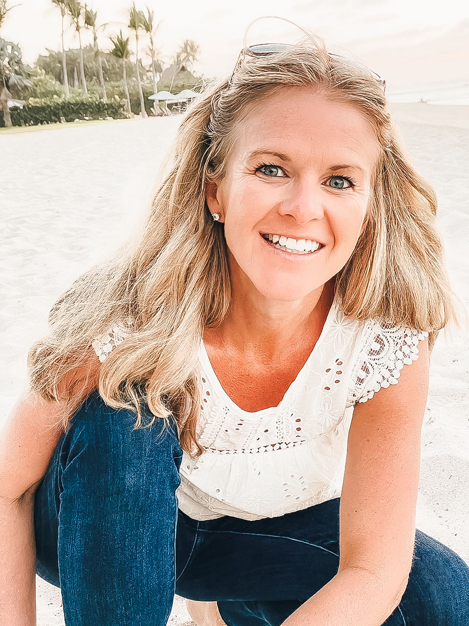 Image of a light-skinned person with long blonde hair kneeling on a beach