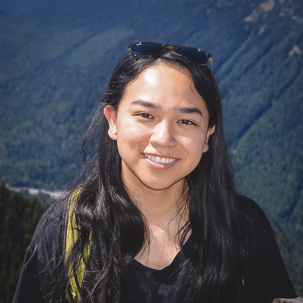 A smiling person with long dark hair posing before a mountain view
