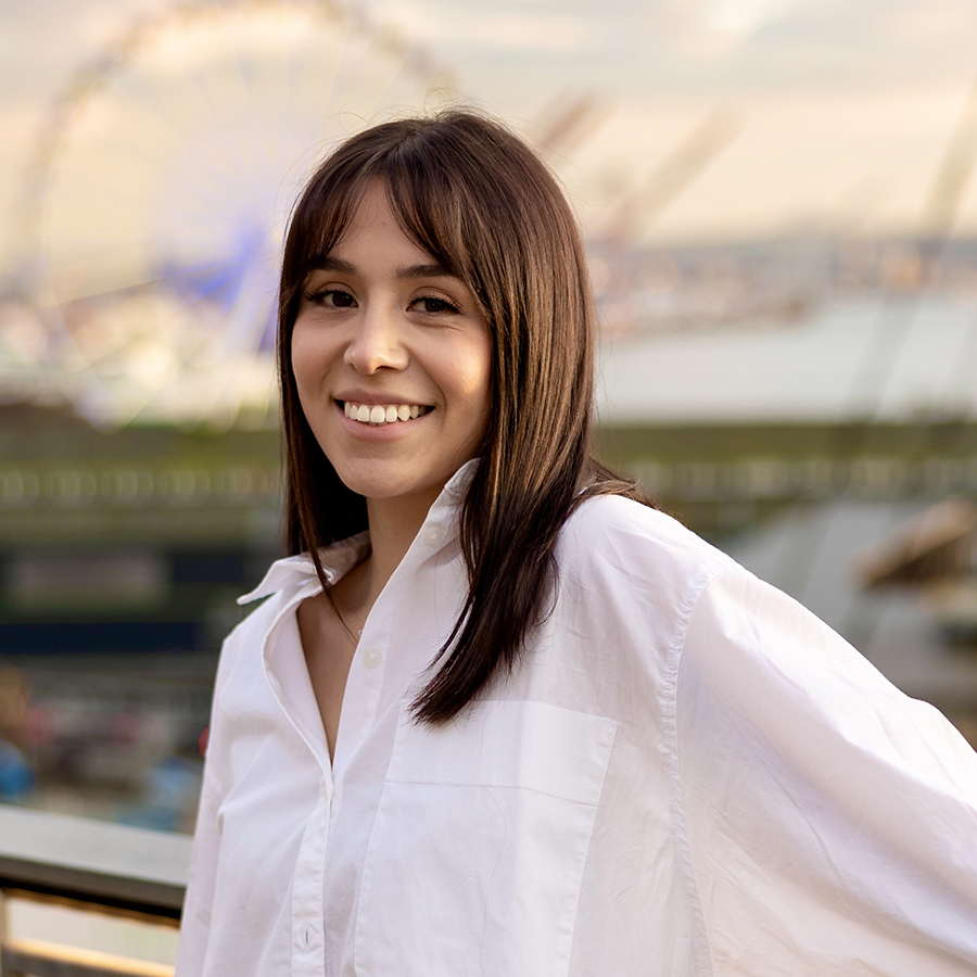 A smiling person with long brown hair poses with a ferris wheel in the background