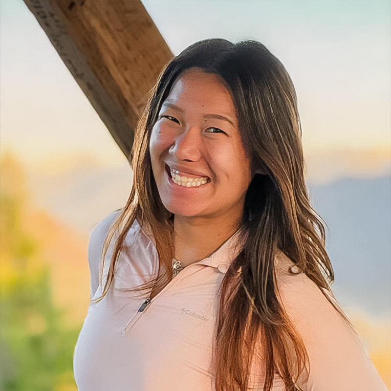 A smiling person with long, brown hair posing outside