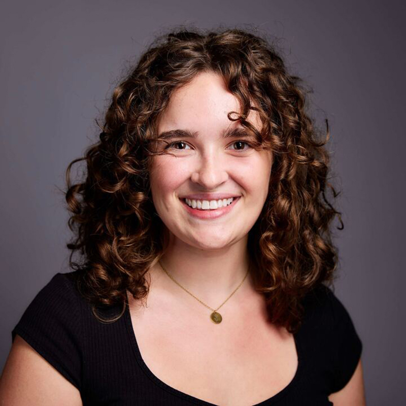 A smiling person with long, brown hair posing outside