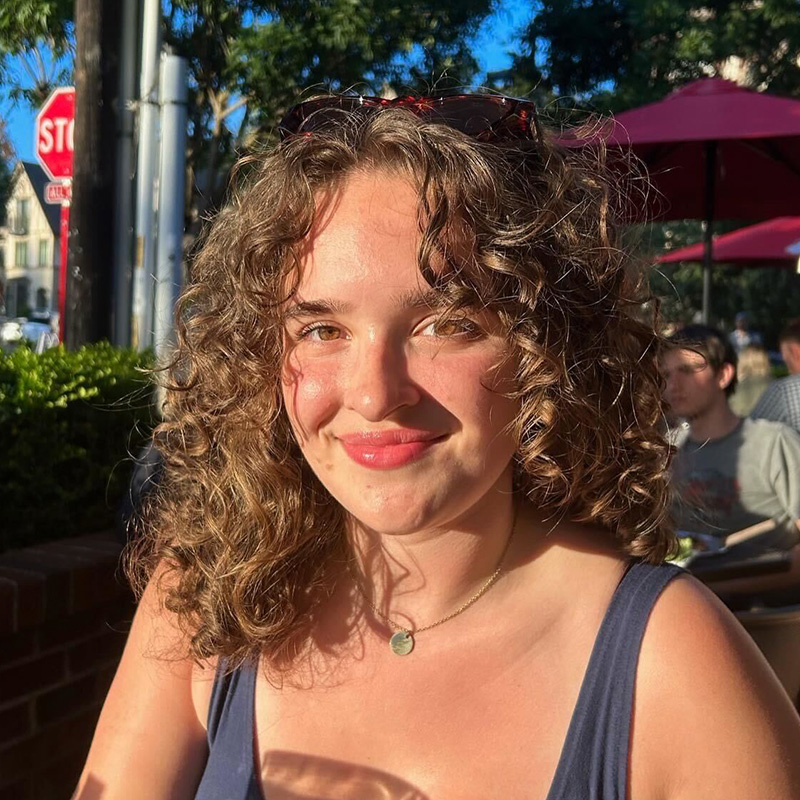A smiling person with shoulder-length brown hair posing before a desert landscape