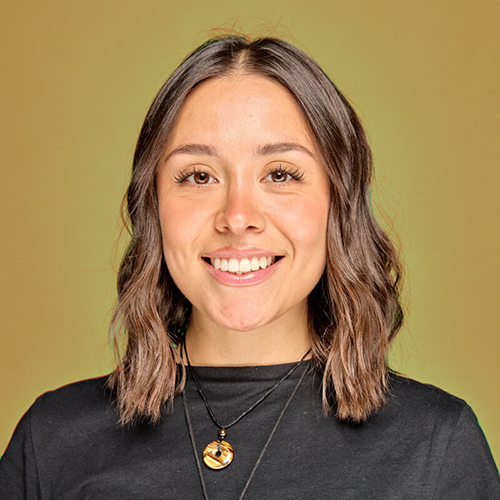 A smiling person with shoulder-length brown hair posing before a desert landscape