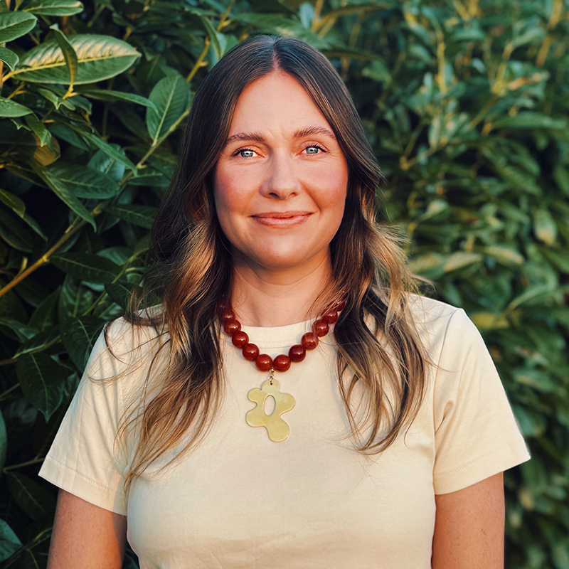 A smiling person with shoulder-length brown hair posing before a desert landscape