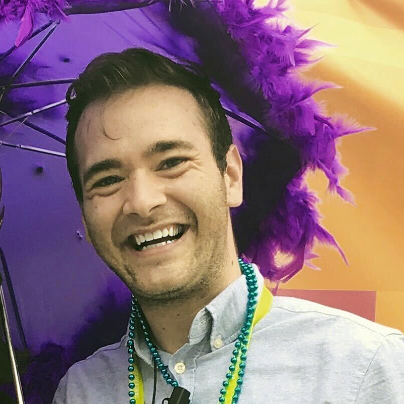 A smiling person with shoulder-length brown hair posing before a desert landscape