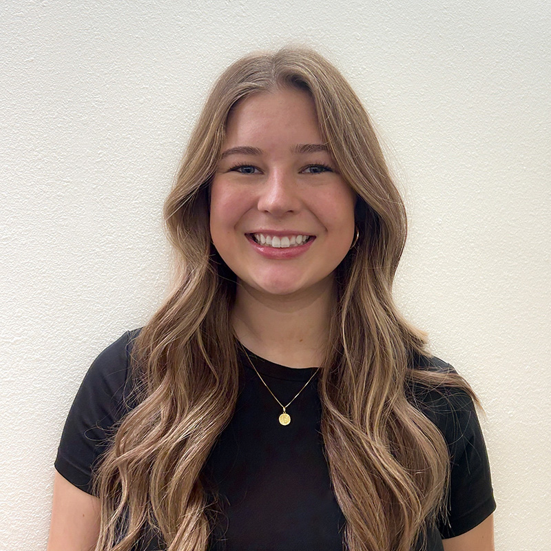 A smiling person with shoulder-length brown hair posing before a desert landscape