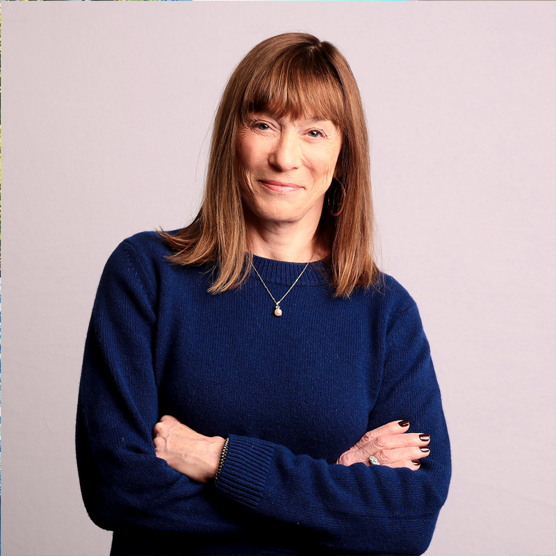 A smiling person with shoulder-length brown hair posing before a desert landscape