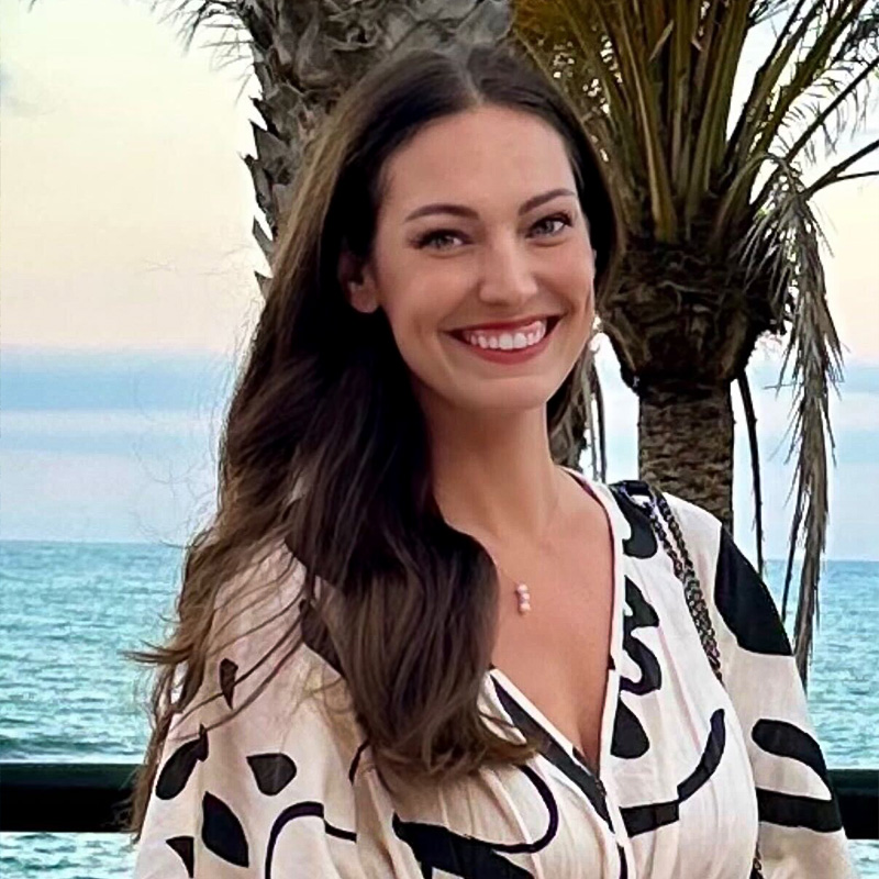 Smiling person with long light brown hair posing before a multicolor background