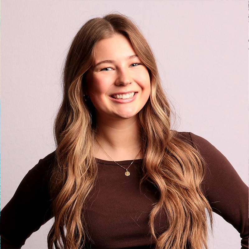 A smiling person with shoulder-length brown hair posing before a desert landscape